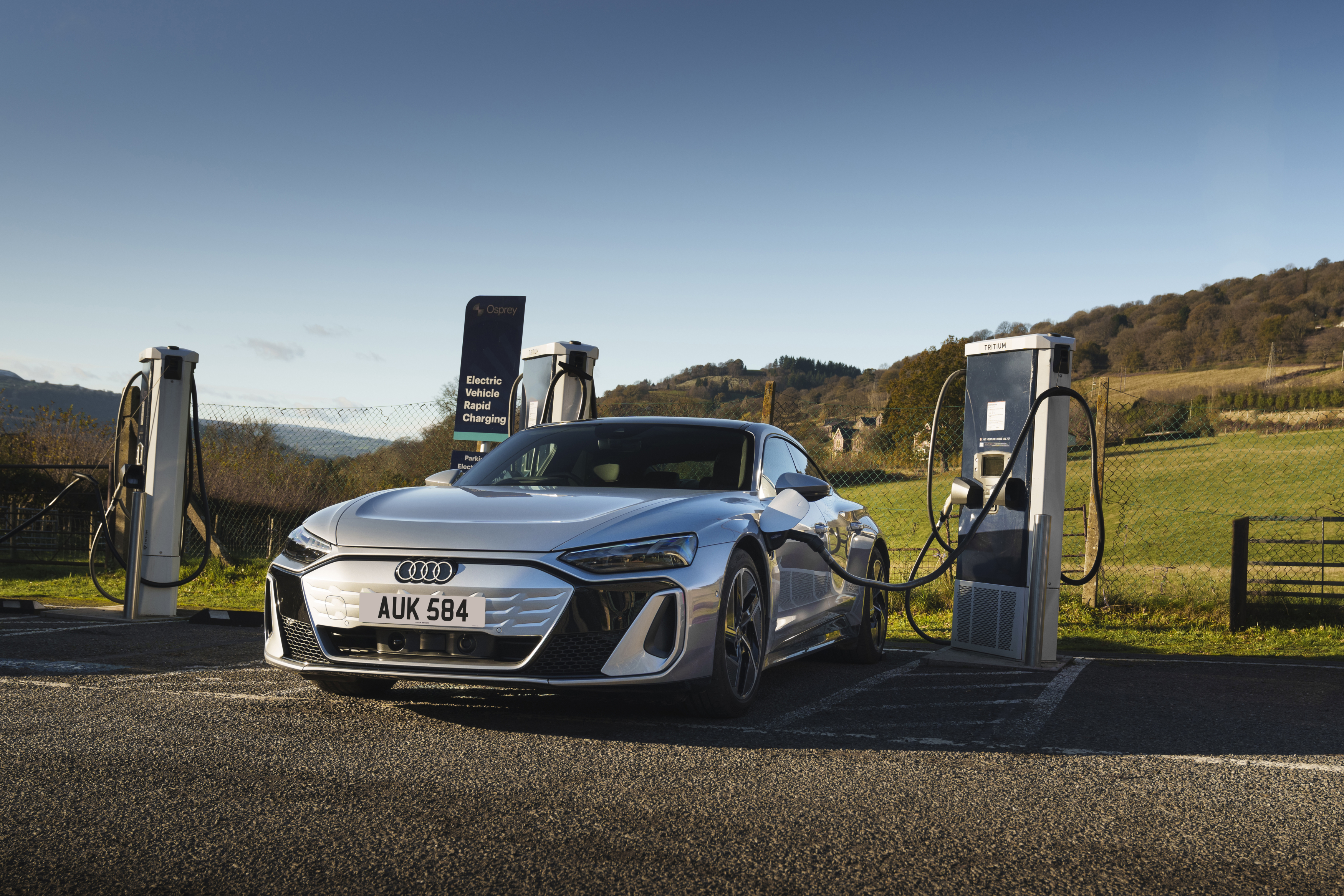Silver Audi electric car charging at a public EV charging station in the countryside.
