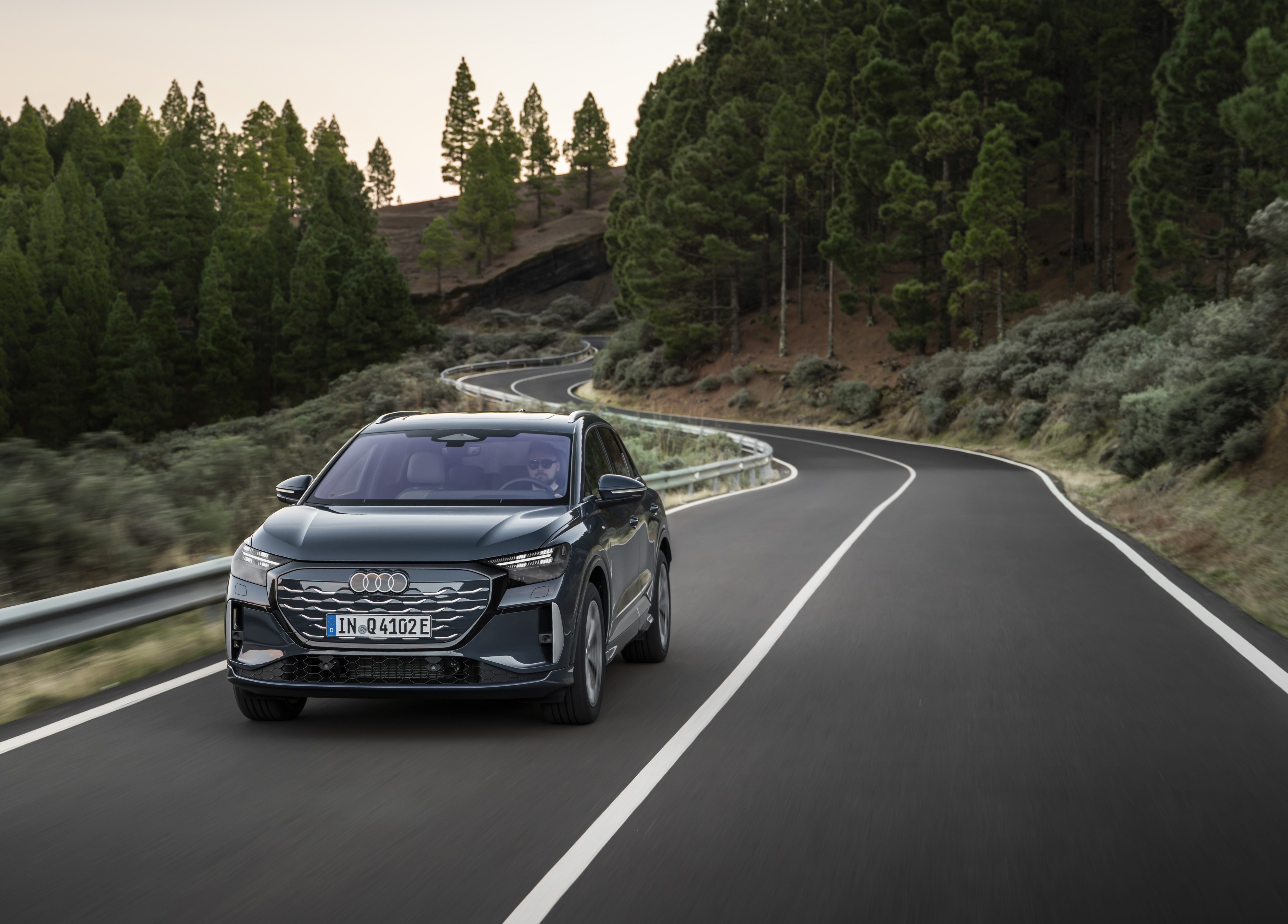 Grey Audi Q4 e-tron driving along a winding mountain road through a forest.