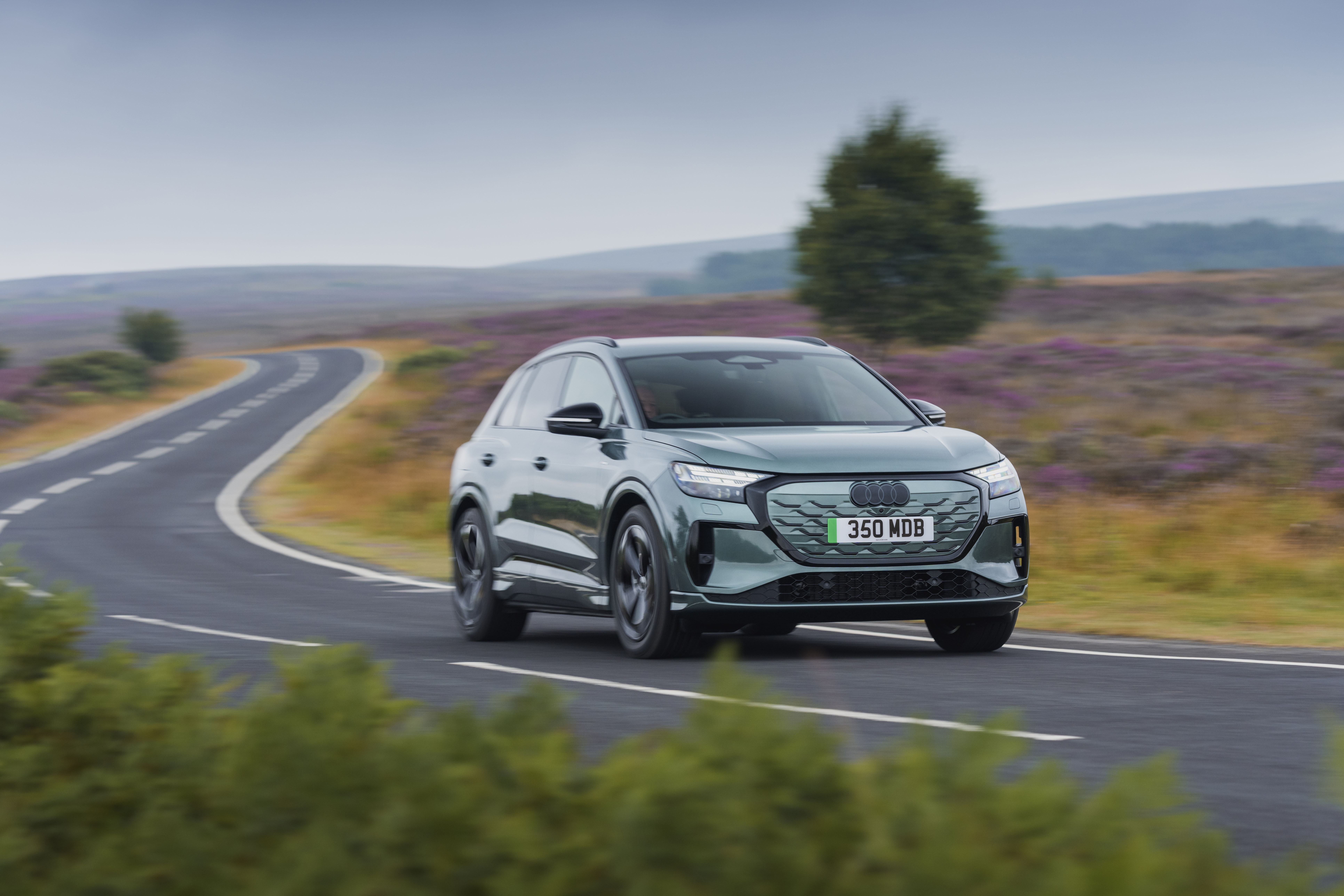 Green Audi Q4 e-tron driving along a winding road through open moorland.