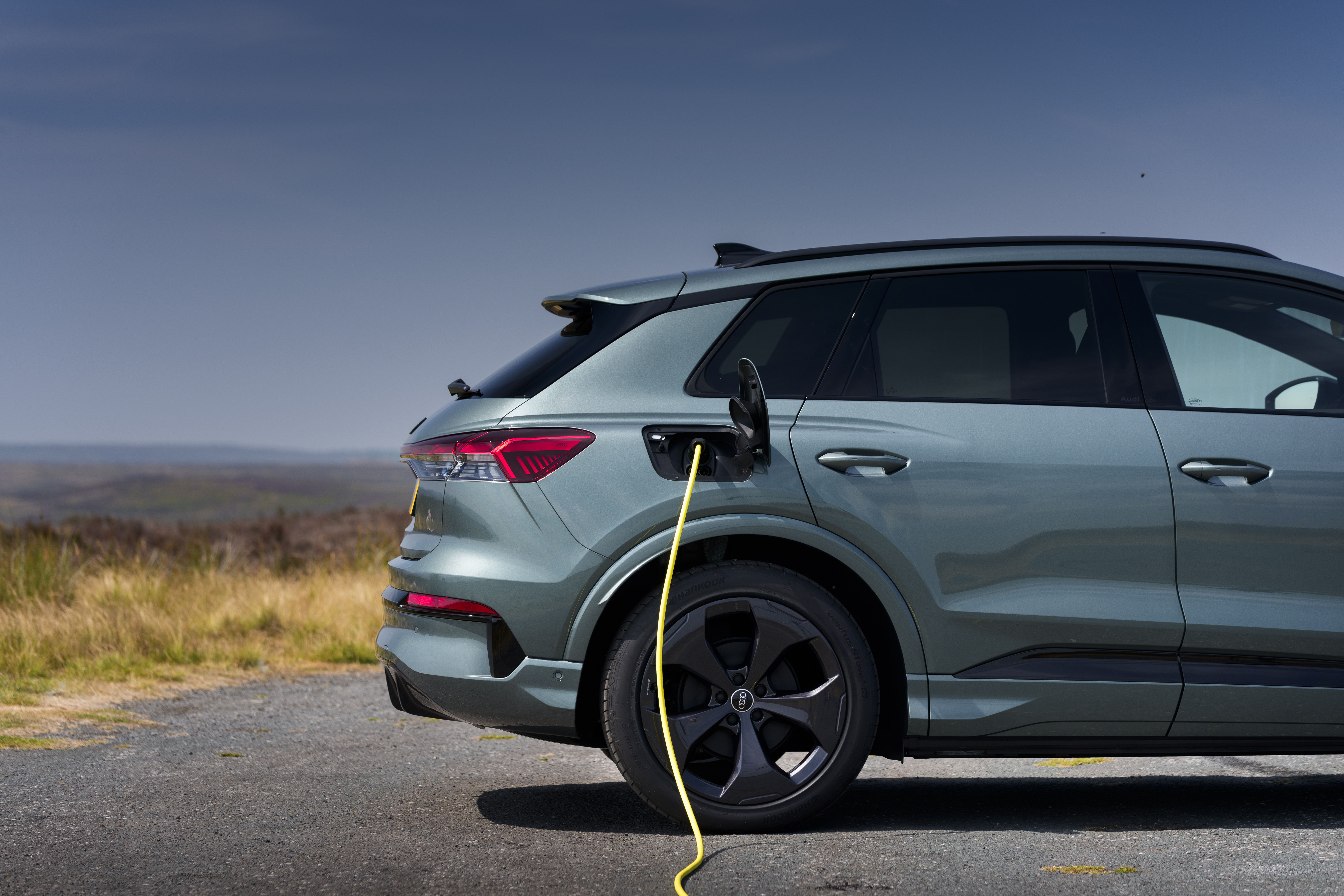 Audi Q4 e-tron electric SUV connected to a charging cable in the countryside.