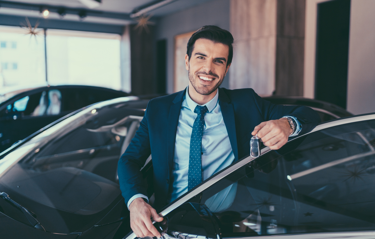 Business Man holding car keys to his new car with door open in car showroom