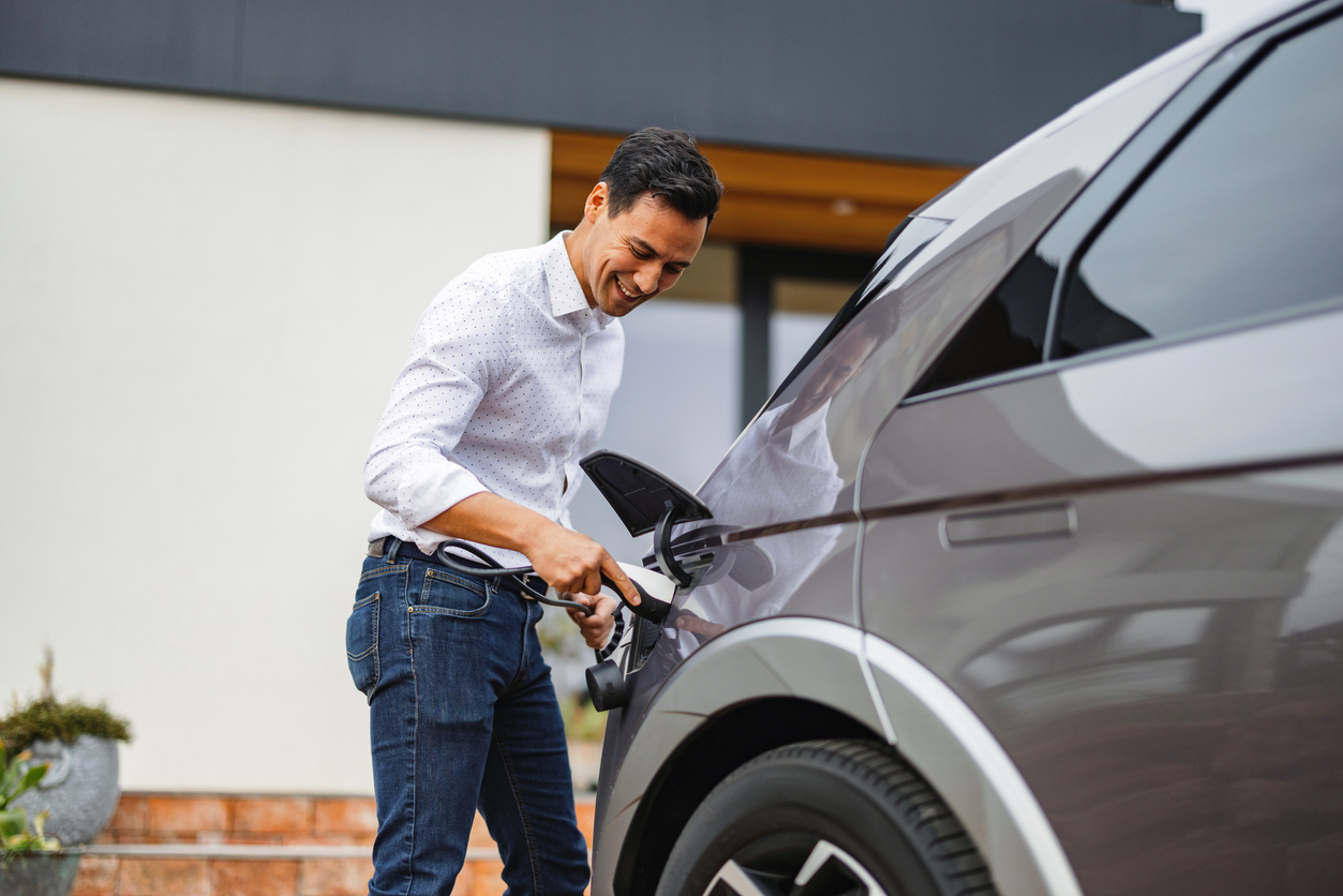 A smart adult businessman happily charges his electric car after returning home from work.