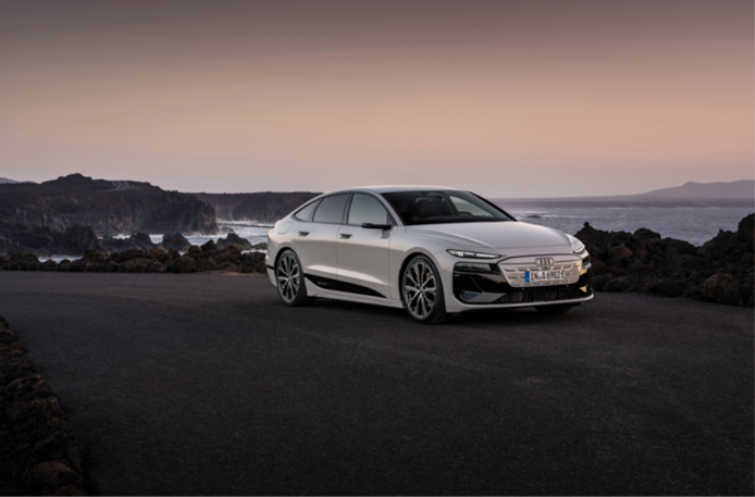 White Audi A6 e-tron parked beside a rocky coastline at sunset.