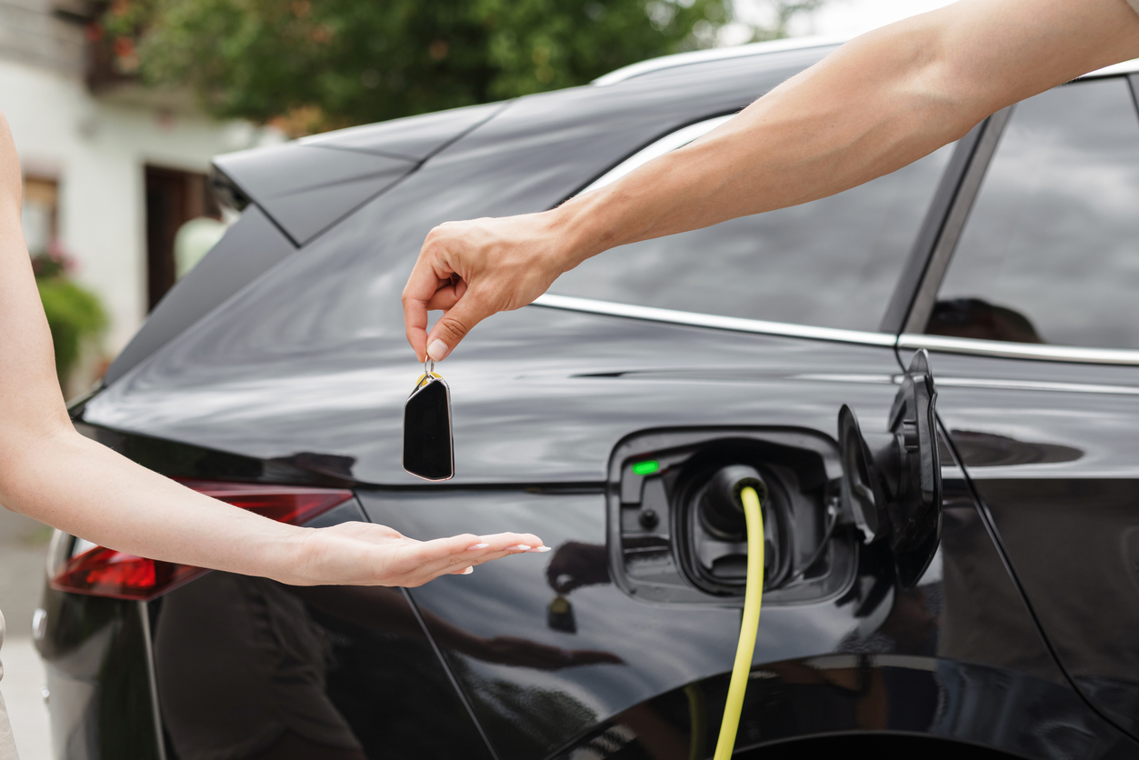 A man handing over car keys to a woman in front of an electric vehicle 