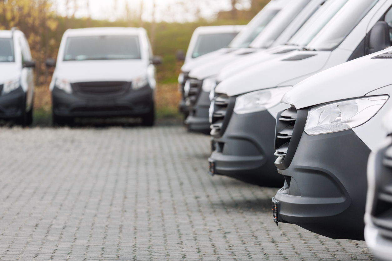 Fleet new modern electric hybrid hydrogen or diesel white vans parked in line row outdoors. 
