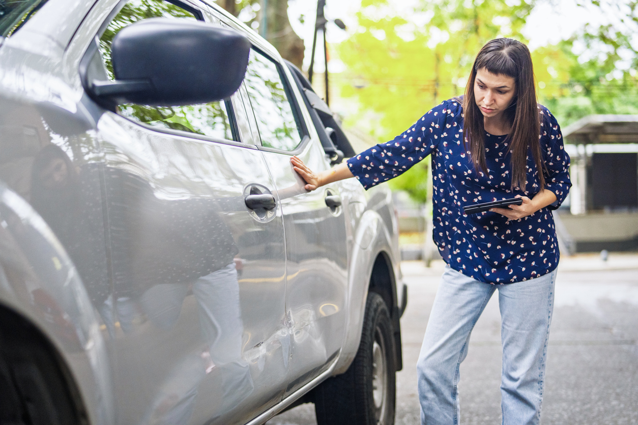 Driver inspecting a dent on a vehicle covered by SMART Insurance for lease cars.